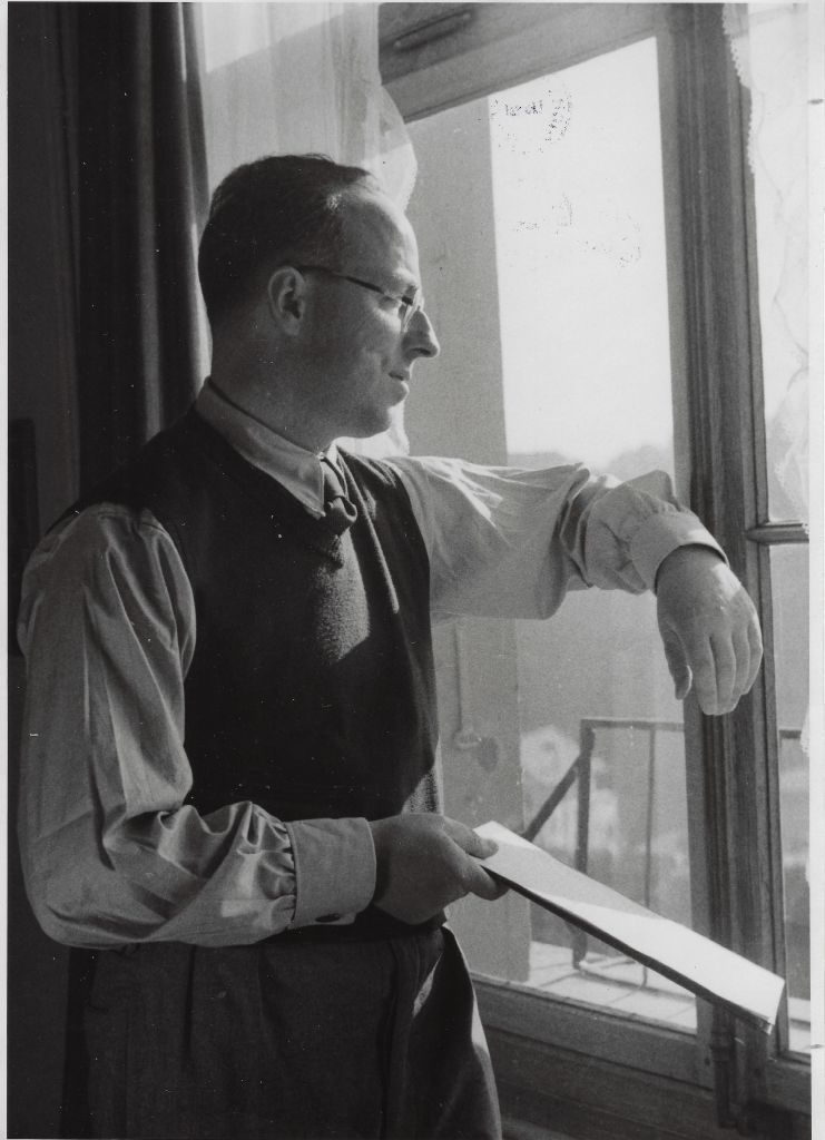Fotografie, Hugo Marti, mit Schreibblock in der Hand, an einem Fenster stehend